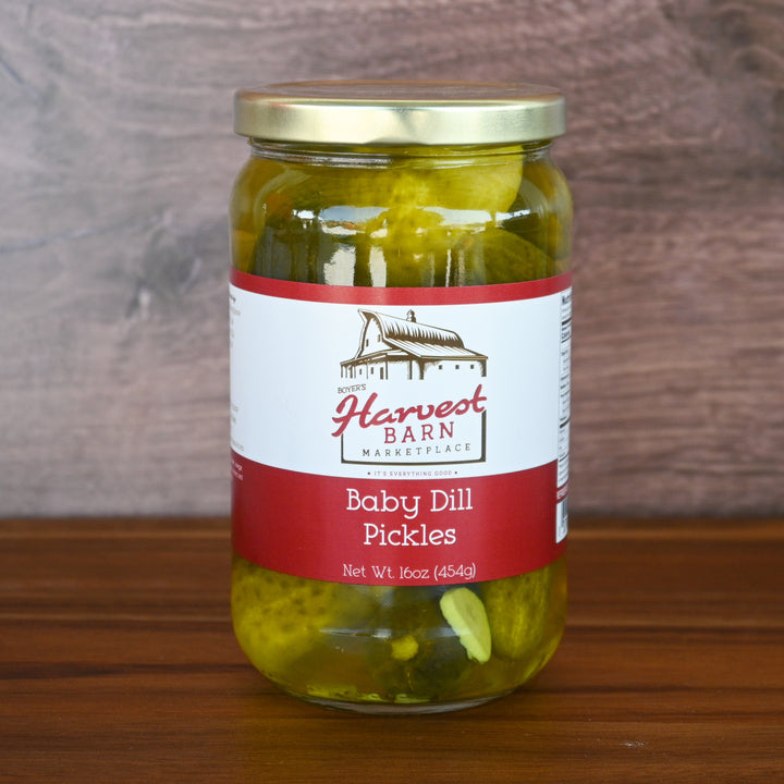 Jar of baby dill pickles with a Harvest Barn label on a wooden surface.