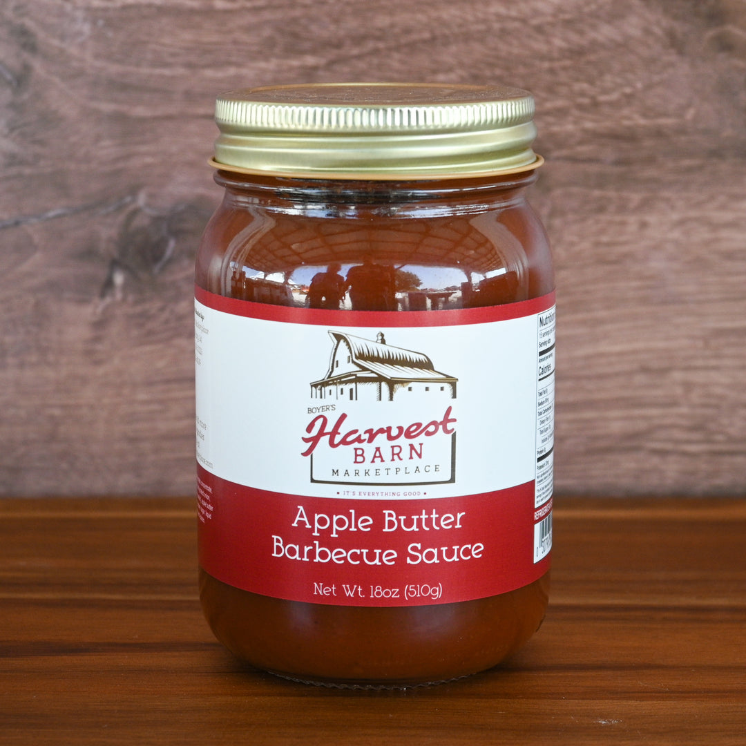 Jar of Apple Butter Barbecue Sauce from Harvest Barn Marketplace on a wooden surface with a wooden background.